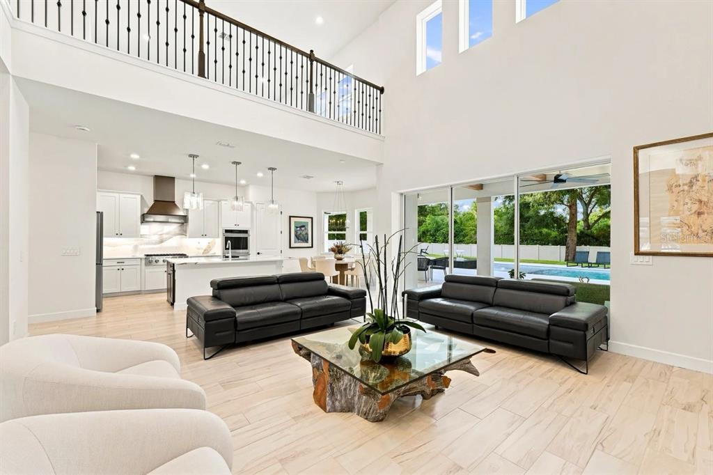 A bright, open-concept living room with black leather sofas, a wood-base coffee table, and pool views — 1113 HOLSTONS POINTE PLACE, GOTHA, FL