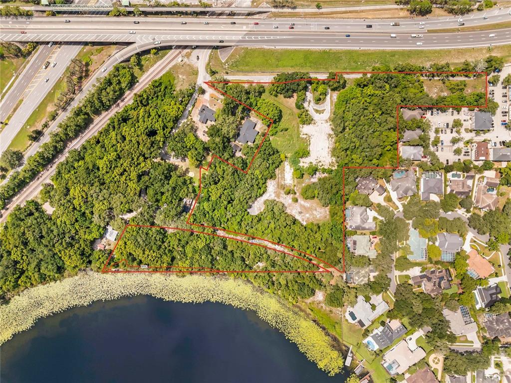 This aerial view shows a wooded lot outlined in red next to a lake and highway — 1250 N MAITLAND AVENUE, MAITLAND, FL