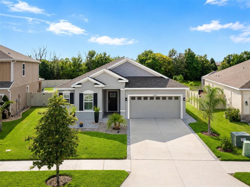 A single-story suburban house with a gray exterior, two-car garage, and a manicured front lawn — 30875 PARROT REEF, WESLEY CHAPEL, FL