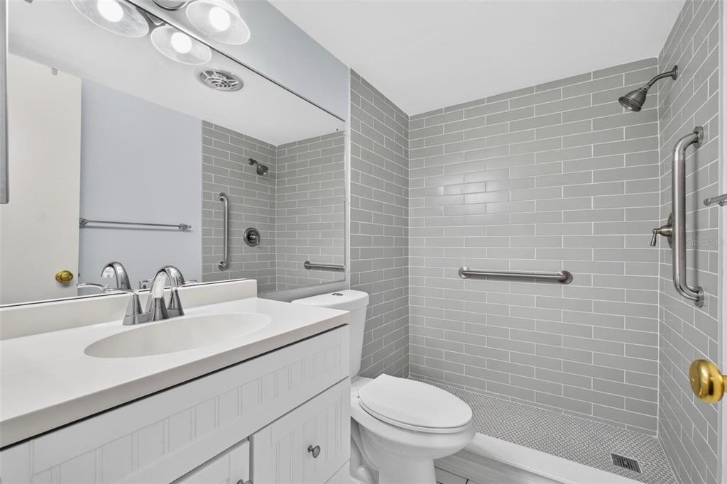 A bathroom features a white vanity, a toilet, and a walk-in shower with gray subway tiles — 138 36TH AVENUE N UNIT 208 W, ST PETERSBURG, FL