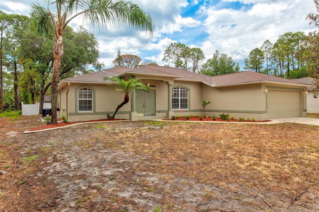 A single-story tan house with a two-car garage and a palm tree in the front yard — 5047 ADINA CIRCLE, NORTH PORT, FL