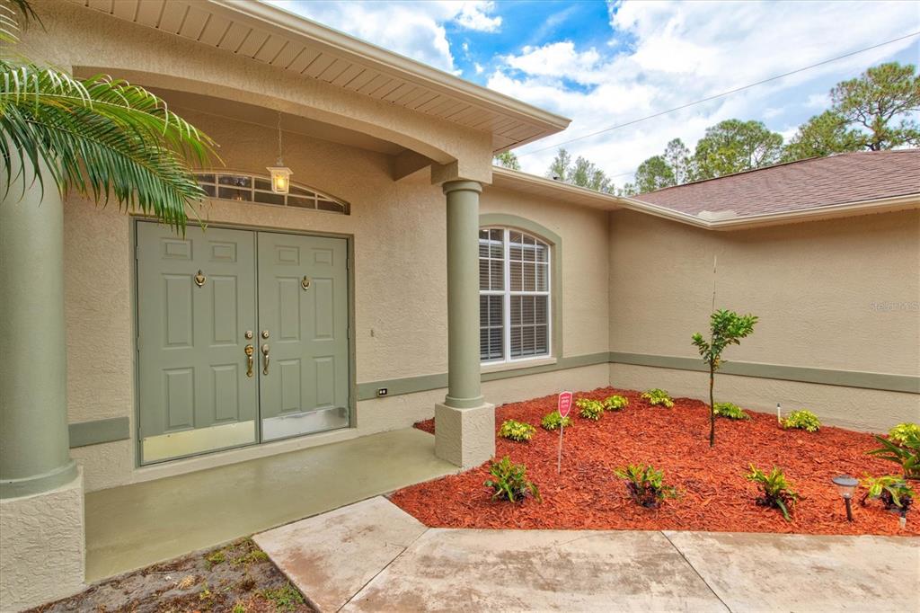 A beige house exterior features a double front door, columns, and a landscaped mulch bed — 5047 ADINA CIRCLE, NORTH PORT, FL