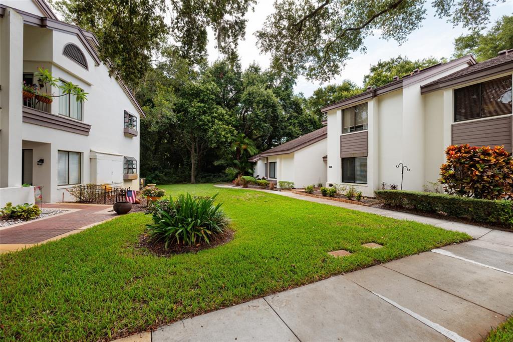 A multi-story residential building with white stucco walls, brown trim, and a landscaped front yard — 1750 LAKE CYPRESS DRIVE UNIT 1002, SAFETY HARBOR, FL