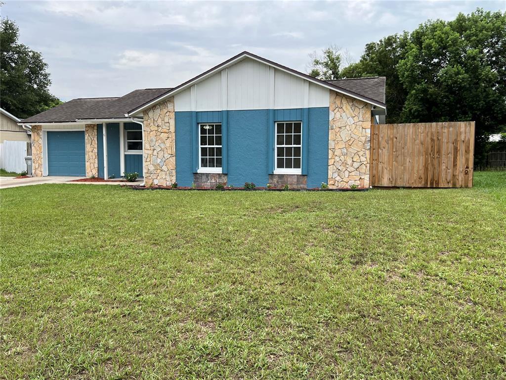 A single-story house features a blue exterior, stone accents, a garage, and a wooden fence — 6 E THRUSH STREET, APOPKA, FL