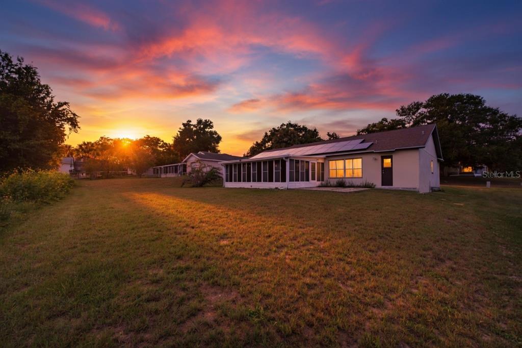 A house with a screened-in porch and solar panels sits on a lawn at sunset — 15904 LAKE ORIENTA COURT, CLERMONT, FL