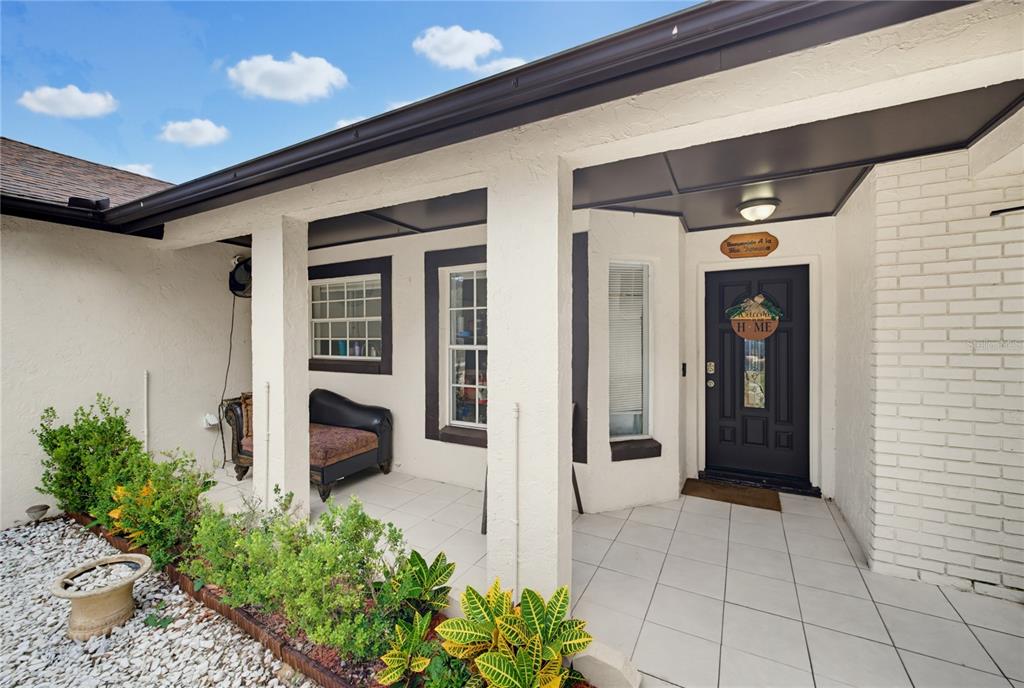 A covered front porch with white tile flooring, a black front door, and landscaping — 15904 LAKE ORIENTA COURT, CLERMONT, FL
