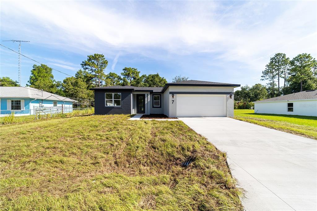 A single-story house with a white garage, dark gray siding, and a concrete driveway — 7 OAK TRAIL, OCALA, FL