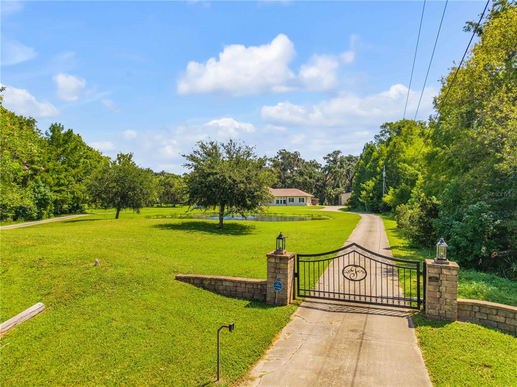 A gated driveway leads to a house situated behind a pond on a grassy lot — 1780 OLD MISSION ROAD, EDGEWATER, FL
