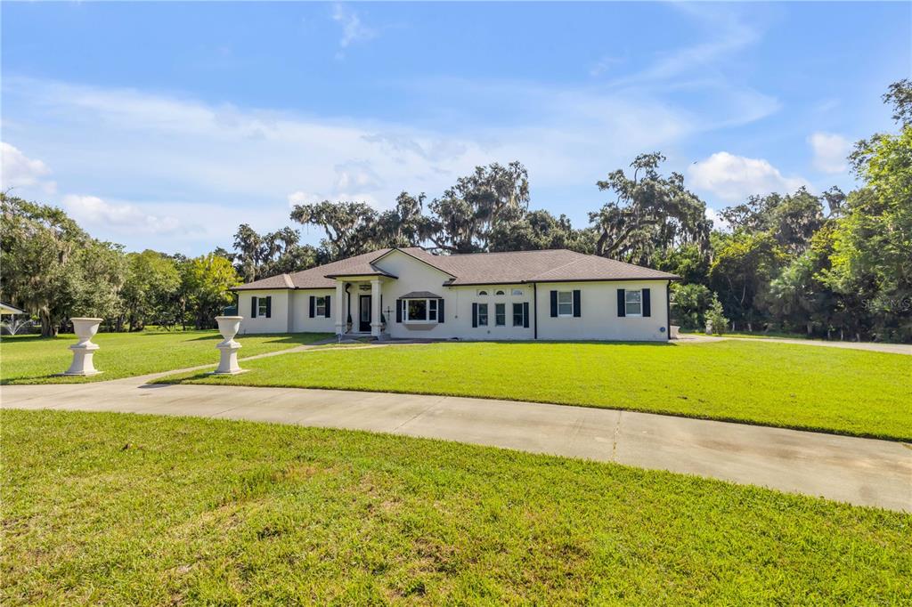 A single-story house with a light-colored exterior sits on a large, grassy lawn — 1780 OLD MISSION ROAD, EDGEWATER, FL