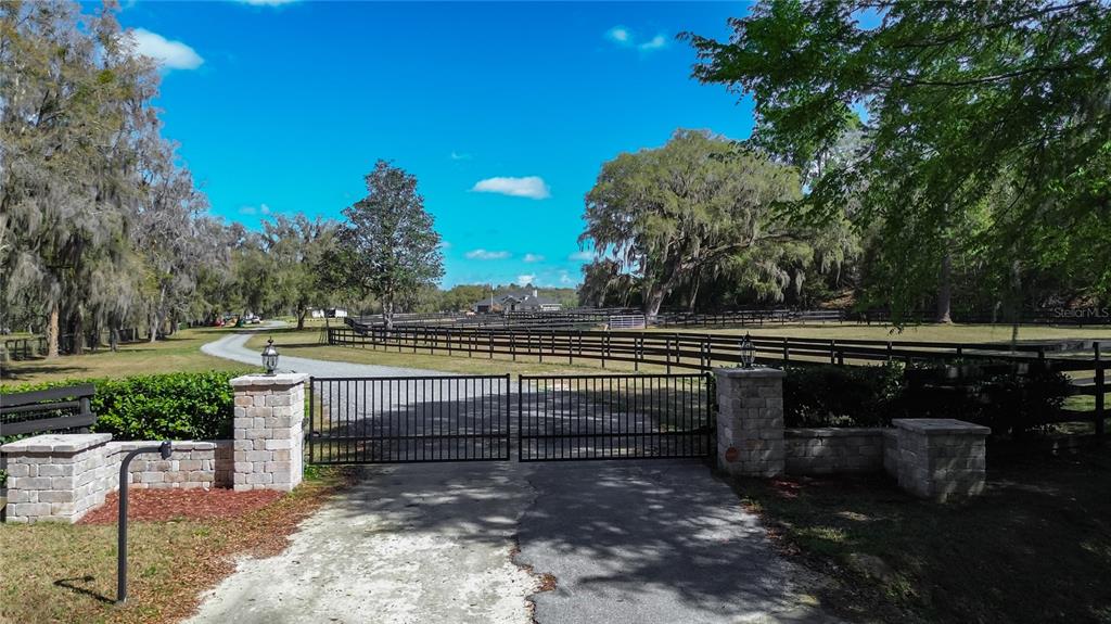 A gated driveway leads to a fenced property with large trees and a distant house — 3245 NW 137TH PLACE, REDDICK, FL