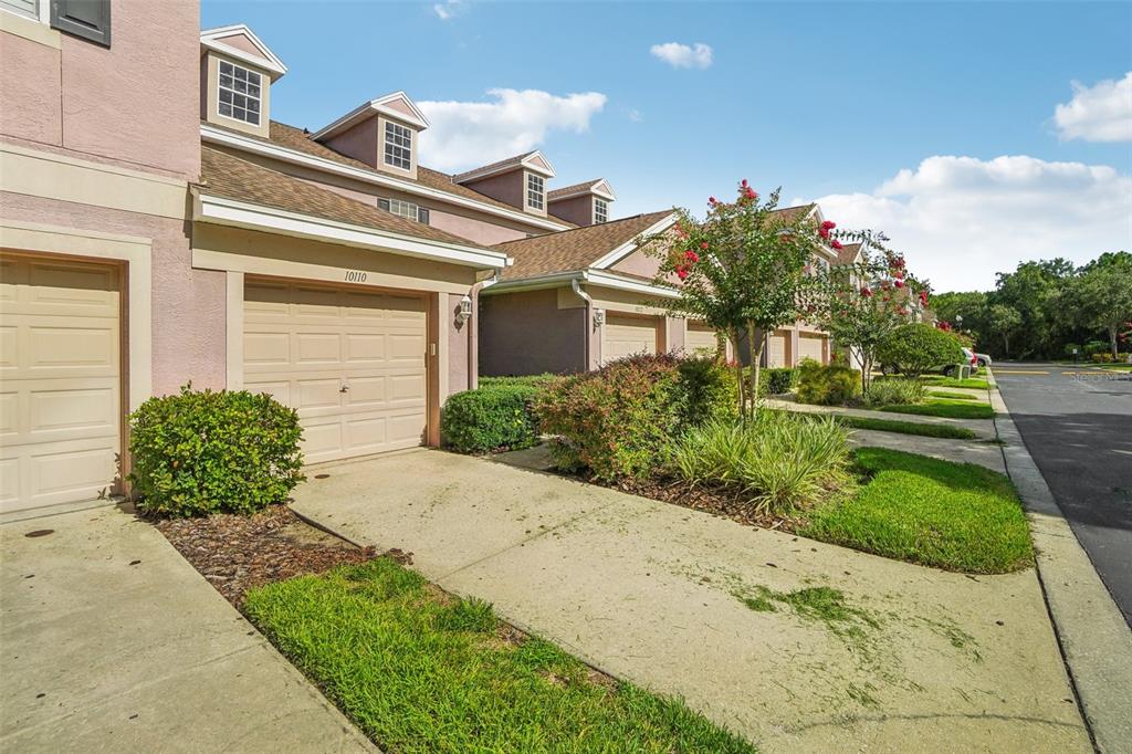 A row of tan townhouses with attached garages and dormer windows under a blue sky — 10110 TRANQUILITY WAY, TAMPA, FL