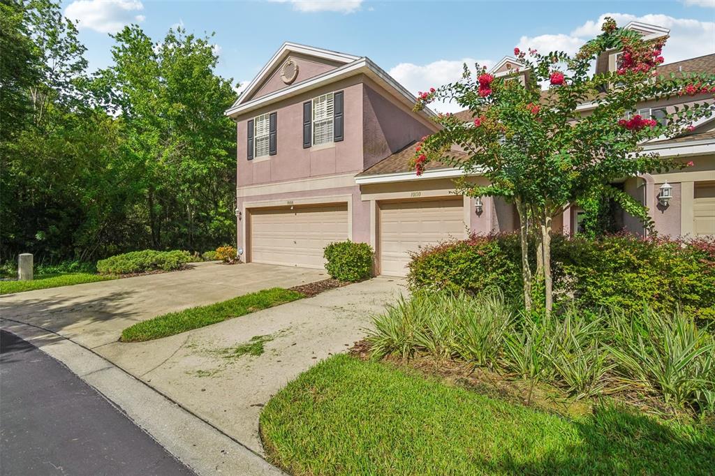 A two-story townhouse with two garage doors, a concrete driveway, and surrounding landscaping — 10110 TRANQUILITY WAY, TAMPA, FL