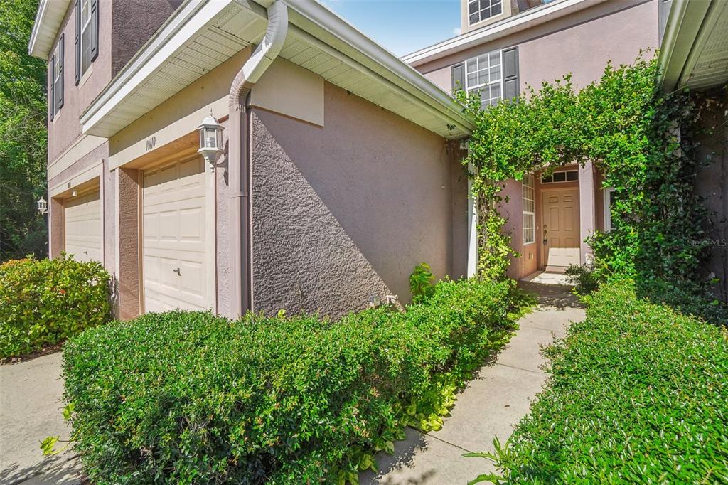 A tan stucco townhouse exterior features a garage, a front entrance, and manicured green hedges — 10110 TRANQUILITY WAY, TAMPA, FL