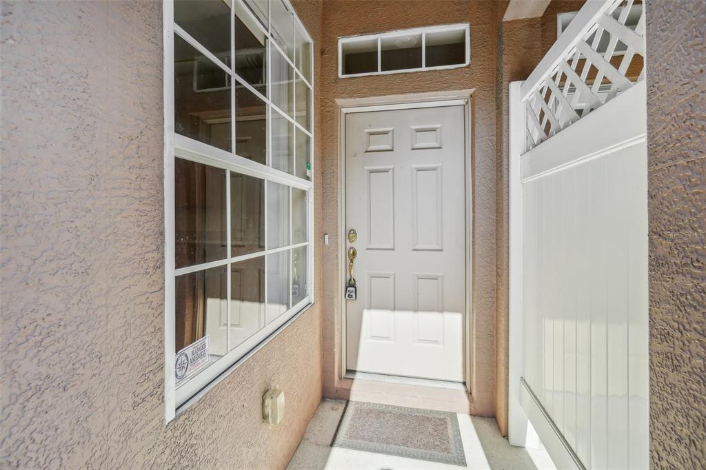 A white front door with a transom window sits beside a window and privacy fence — 10110 TRANQUILITY WAY, TAMPA, FL