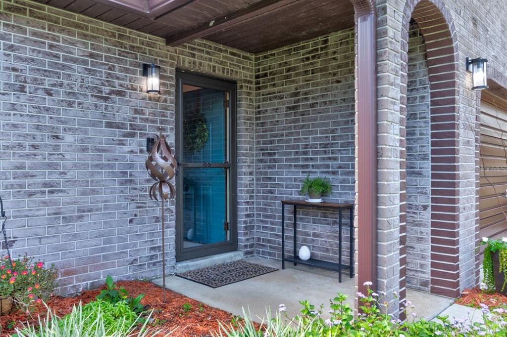 A front porch with a brick exterior, a glass storm door, and a small console table — 16 LAUREL OAKS CIRCLE, ORMOND BEACH, FL