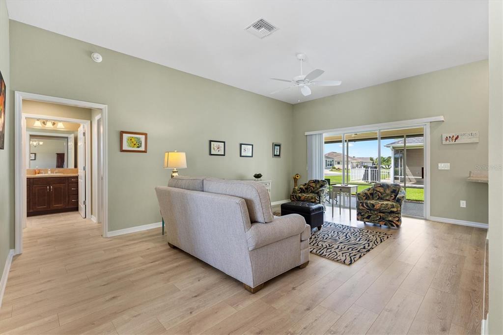 A living room with light wood floors, sage green walls, and sliding glass doors — 3602 PEPPERIDGE CIRCLE, THE VILLAGES, FL