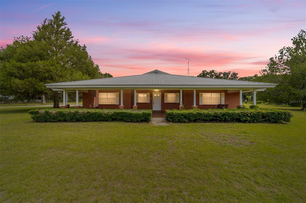 A single-story brick house with a metal roof and a wide front porch at sunset — 2285 W HIGHWAY 318, CITRA, FL