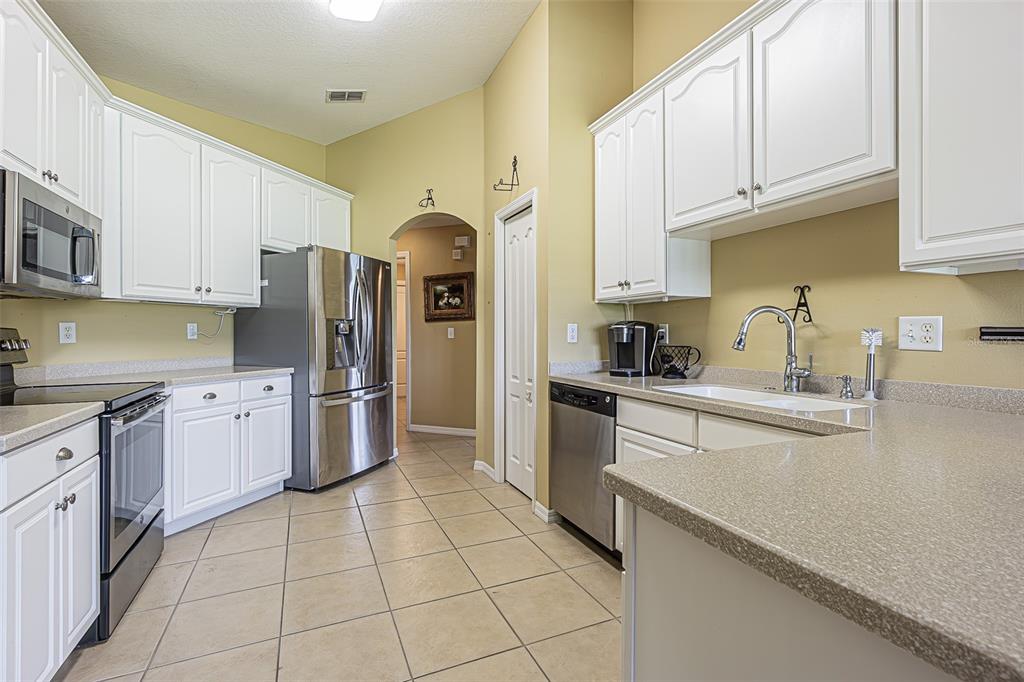 A kitchen features white cabinets, stainless steel appliances, tan countertops, and light-colored tile flooring — 29435 SNAP HOOK DRIVE, SAN ANTONIO, FL