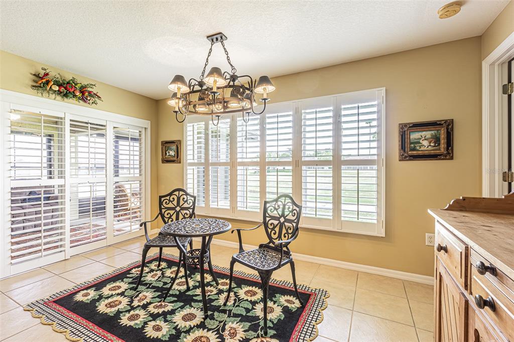 A dining area features a round table, two chairs, a sunflower rug, and plantation shutters — 29435 SNAP HOOK DRIVE, SAN ANTONIO, FL