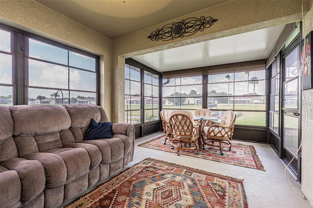 A sunroom features a brown sofa, a dining set on a rug, and large windows — 29435 SNAP HOOK DRIVE, SAN ANTONIO, FL