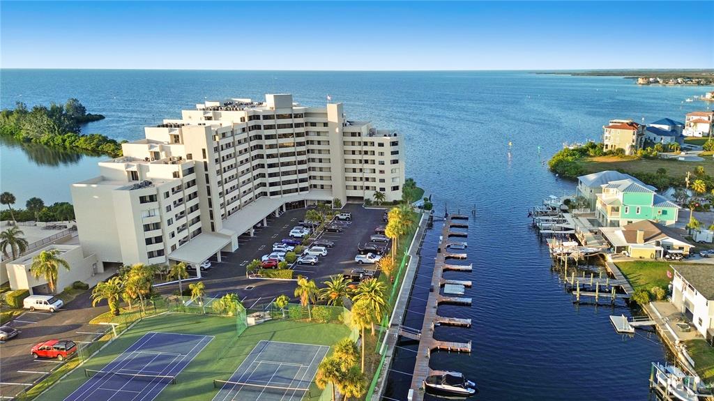 An aerial view shows a multi-story apartment building, a parking lot, tennis courts, and docks — 6035 SEA RANCH DRIVE UNIT 203, HUDSON, FL