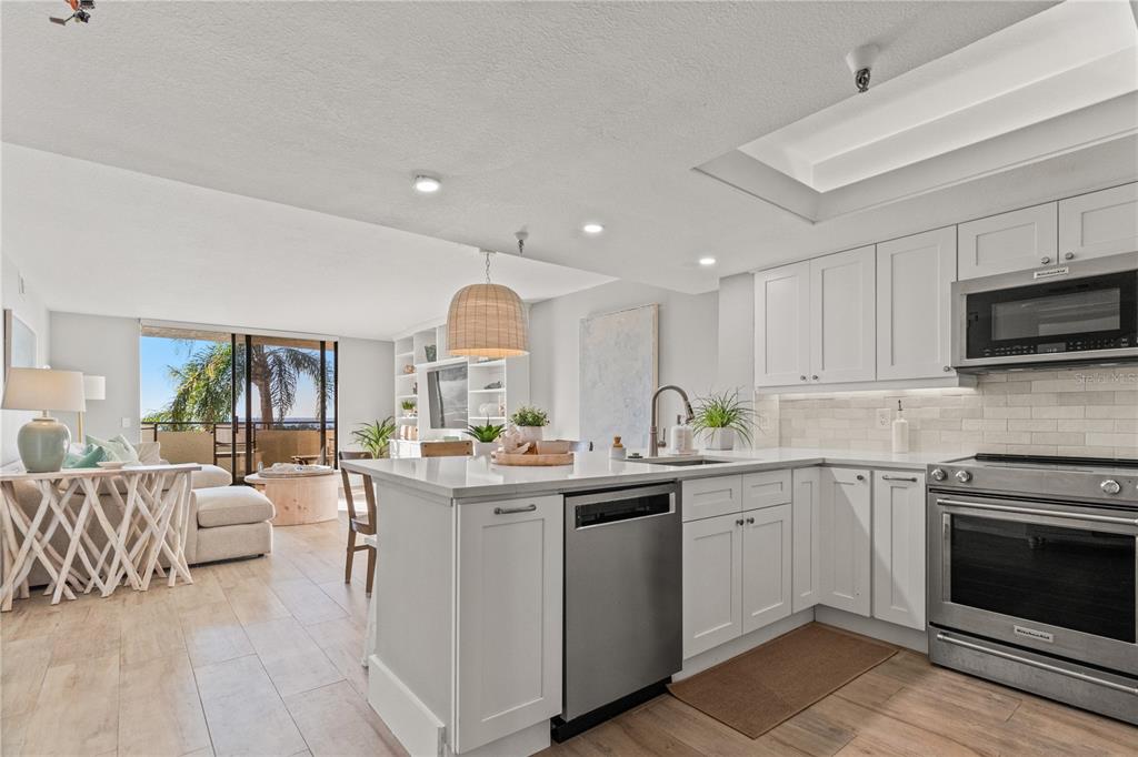 A modern kitchen with white cabinets and stainless steel appliances opens to a bright living area — 6035 SEA RANCH DRIVE UNIT 203, HUDSON, FL