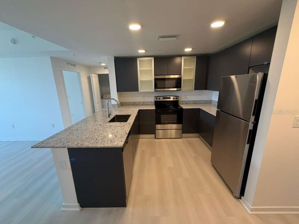 A modern kitchen features dark cabinetry, granite countertops, and stainless steel appliances — 5587 MILLENIA PARK BOULEVARD UNIT 409, ORLANDO, FL