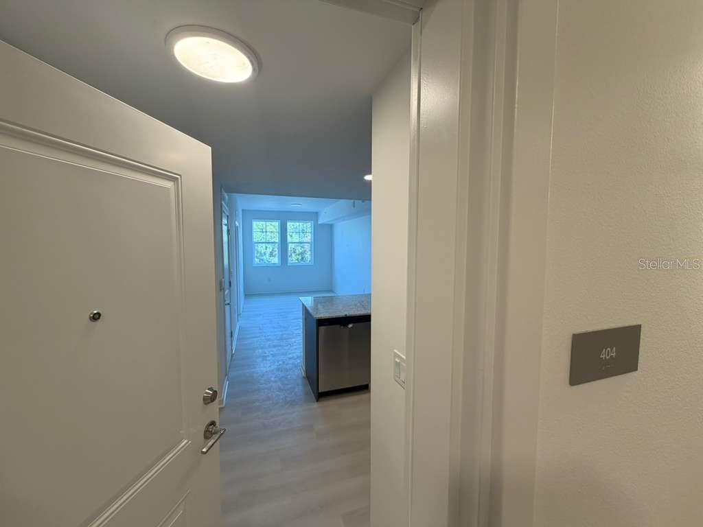 A view through an open doorway into an apartment unit with light wood-look flooring — 5587 MILLENIA PARK BOULEVARD UNIT 409, ORLANDO, FL