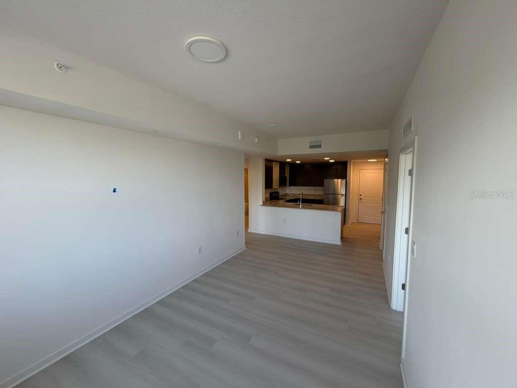An open-concept living area features light wood-look flooring and a view into the kitchen — 5587 MILLENIA PARK BOULEVARD UNIT 409, ORLANDO, FL