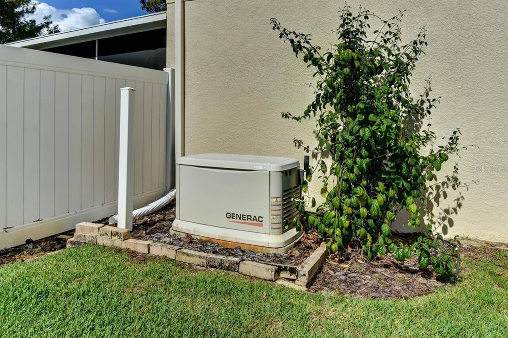 A Generac standby generator sits on a brick-bordered pad next to a house wall — 831 OAK HOLLOW LOOP, DELAND, FL