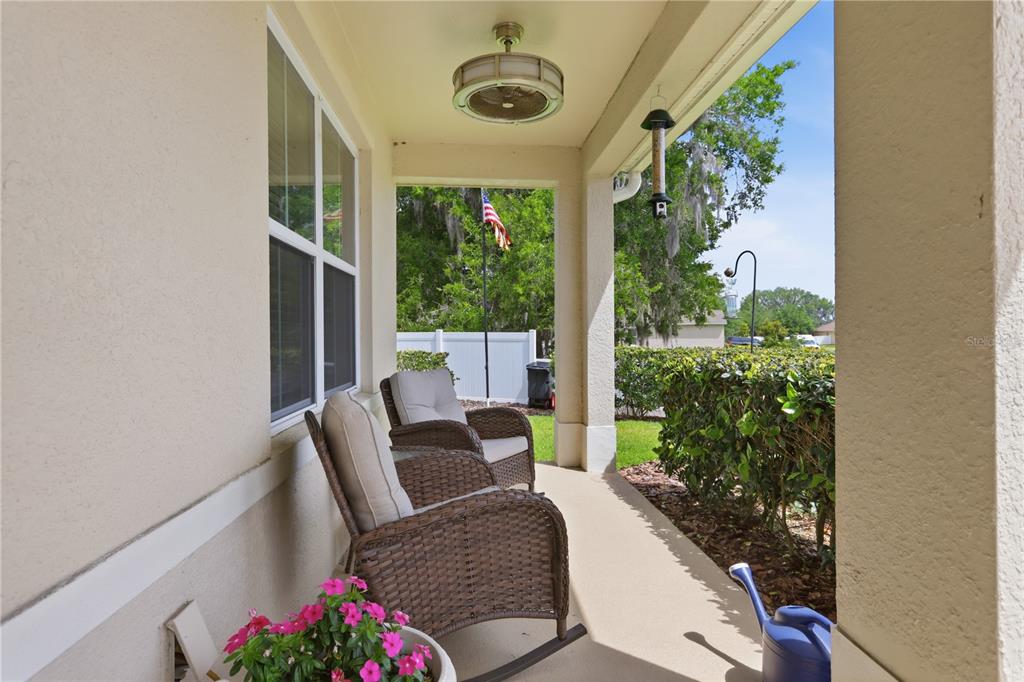 A covered front porch features two wicker rocking chairs, a ceiling fan, and potted flowers — 831 OAK HOLLOW LOOP, DELAND, FL