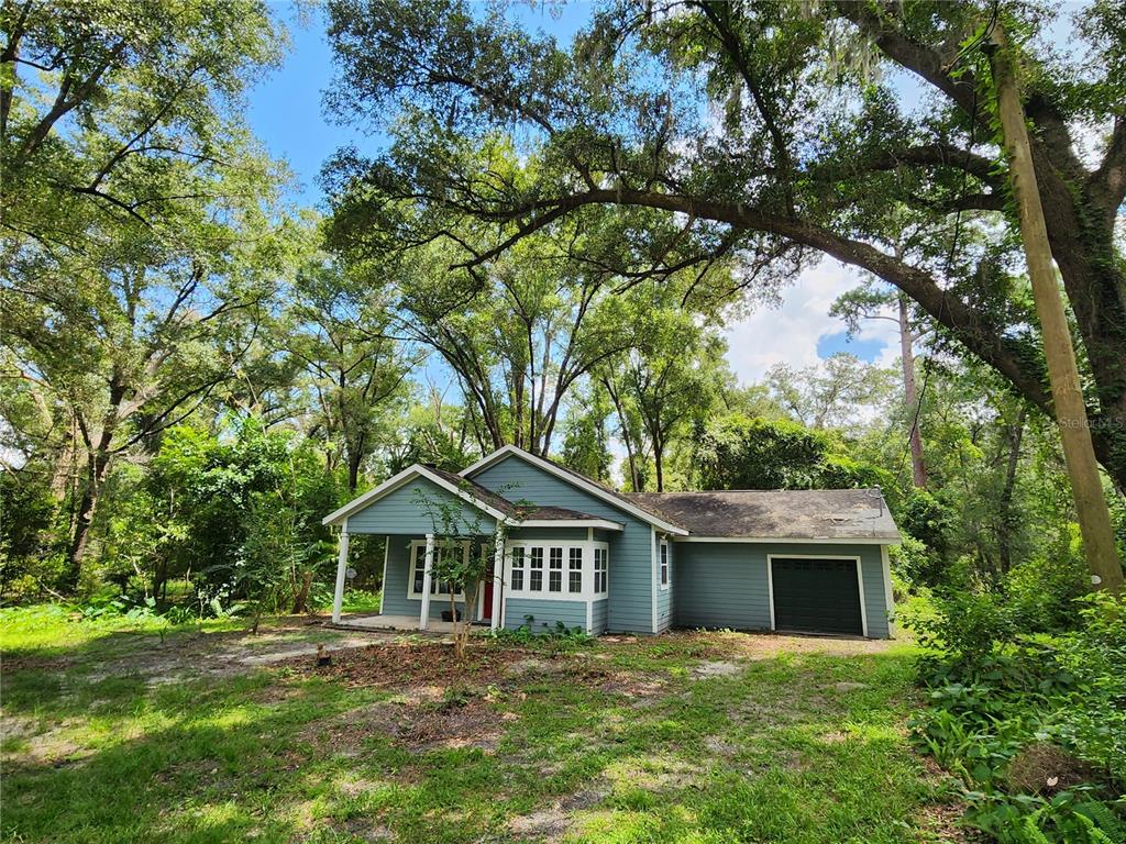A blue single-story house with a front porch and an attached garage sits among trees — 8909 SE 2ND STREET ROAD, TRENTON, FL