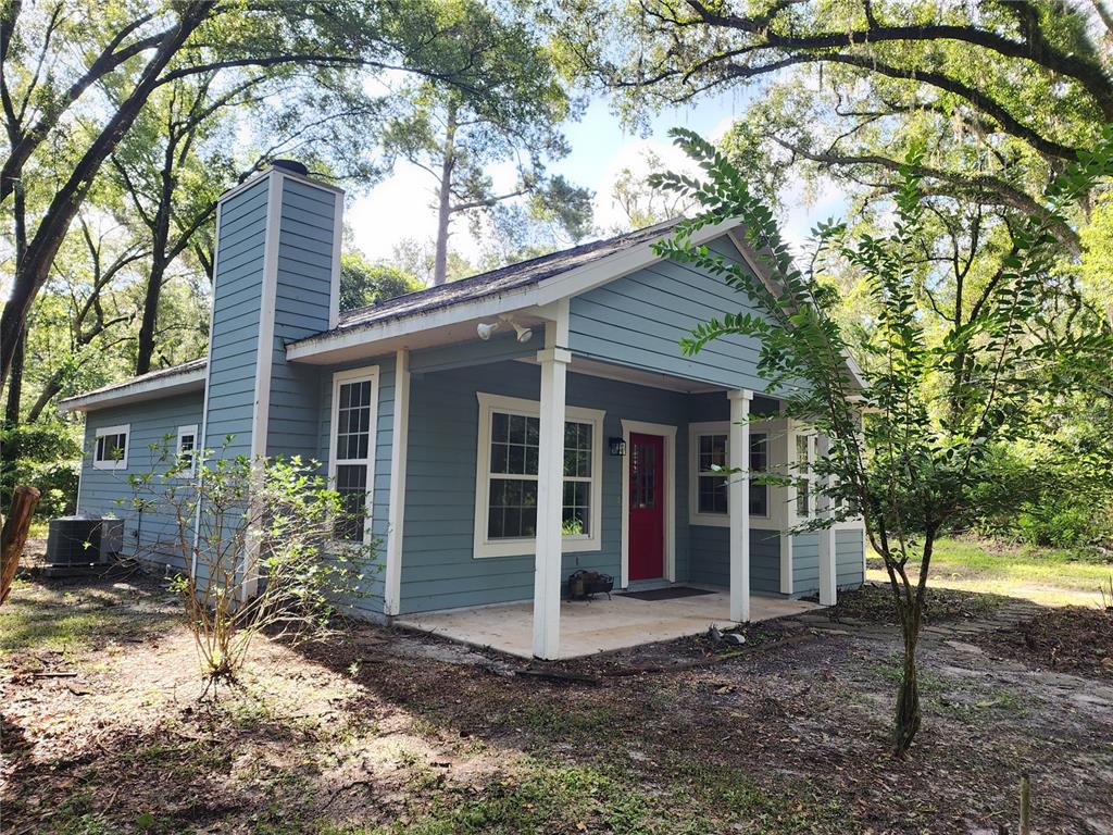 A blue-sided cottage with a red front door, a front porch, and a brick chimney — 8909 SE 2ND STREET ROAD, TRENTON, FL