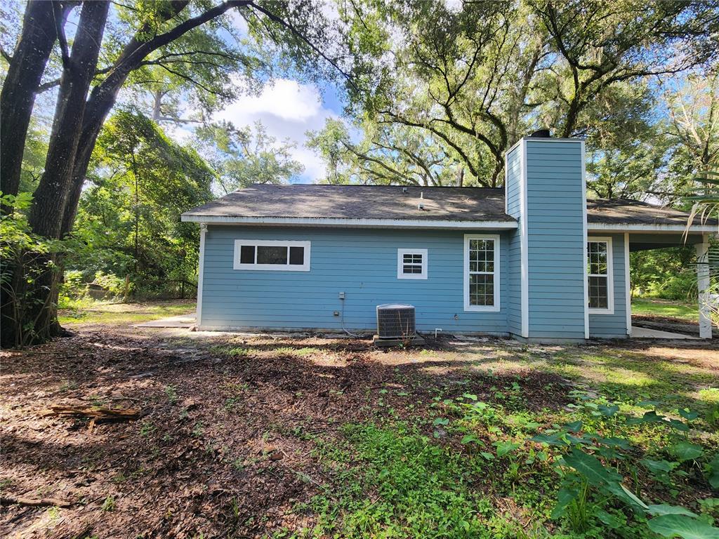 The exterior of a blue-sided house features a chimney, an air conditioning unit, and windows — 8909 SE 2ND STREET ROAD, TRENTON, FL