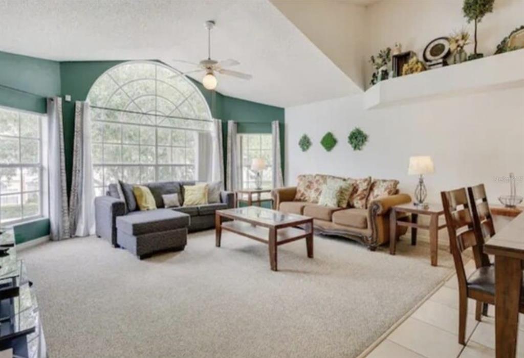 A living room with a vaulted ceiling, large arched window, carpeted flooring, and two sofas — 5004 LAGUNA BAY CIRCLE UNIT 54, KISSIMMEE, FL