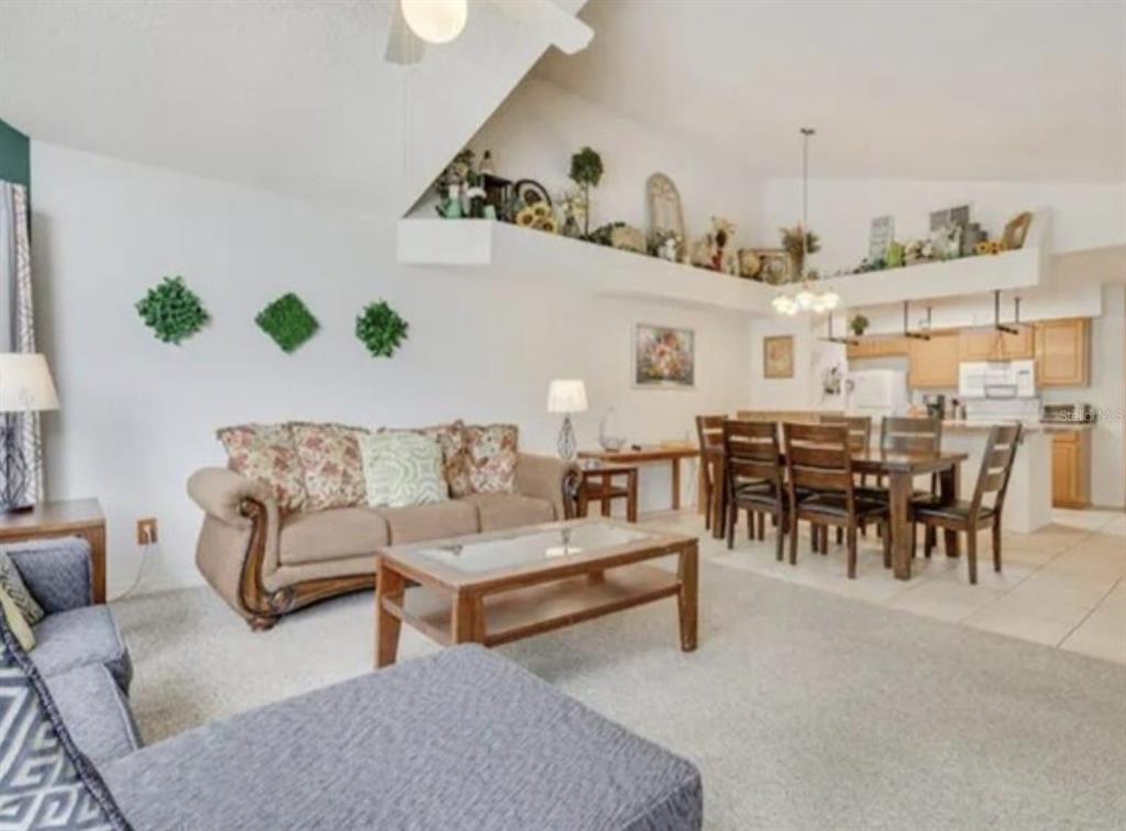 A living room with a vaulted ceiling, carpeted floors, and an adjacent dining area — 5004 LAGUNA BAY CIRCLE UNIT 54, KISSIMMEE, FL