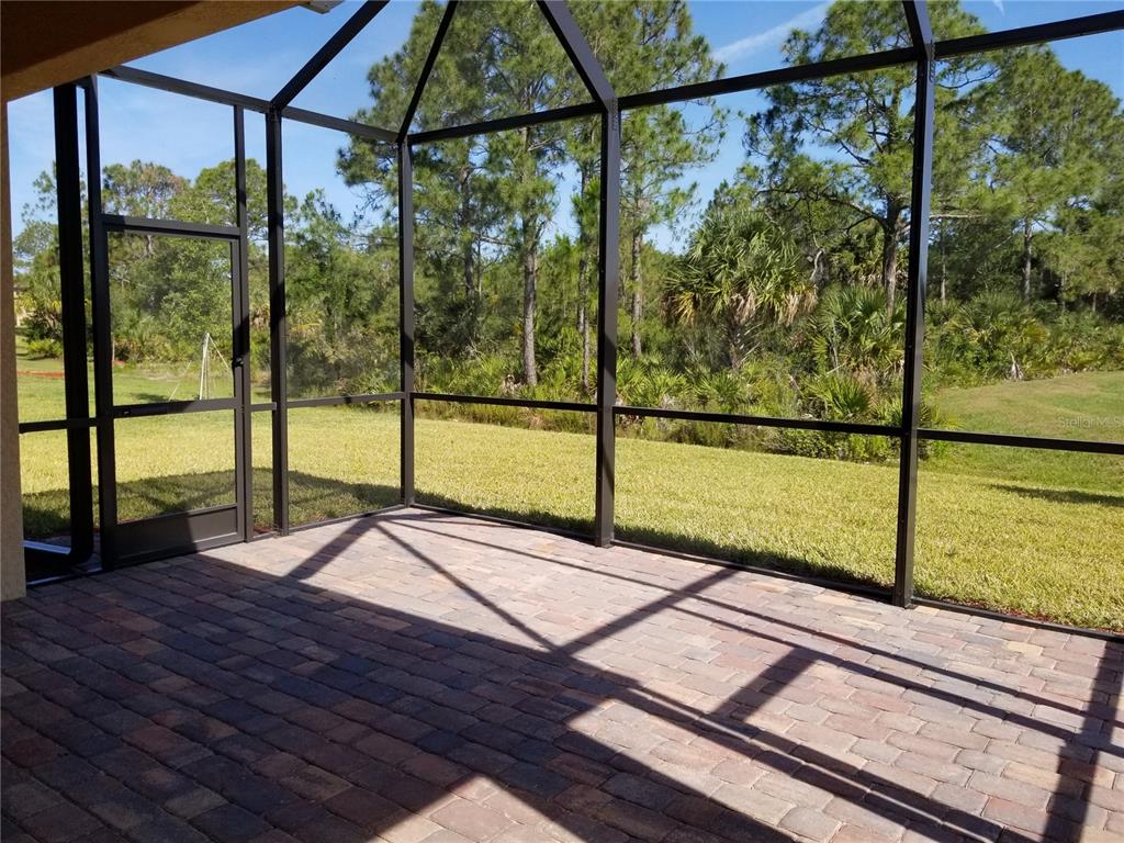 A screened-in patio with brick pavers overlooks a grassy yard and a line of trees — 12324 CANAVESE LANE, VENICE, FL