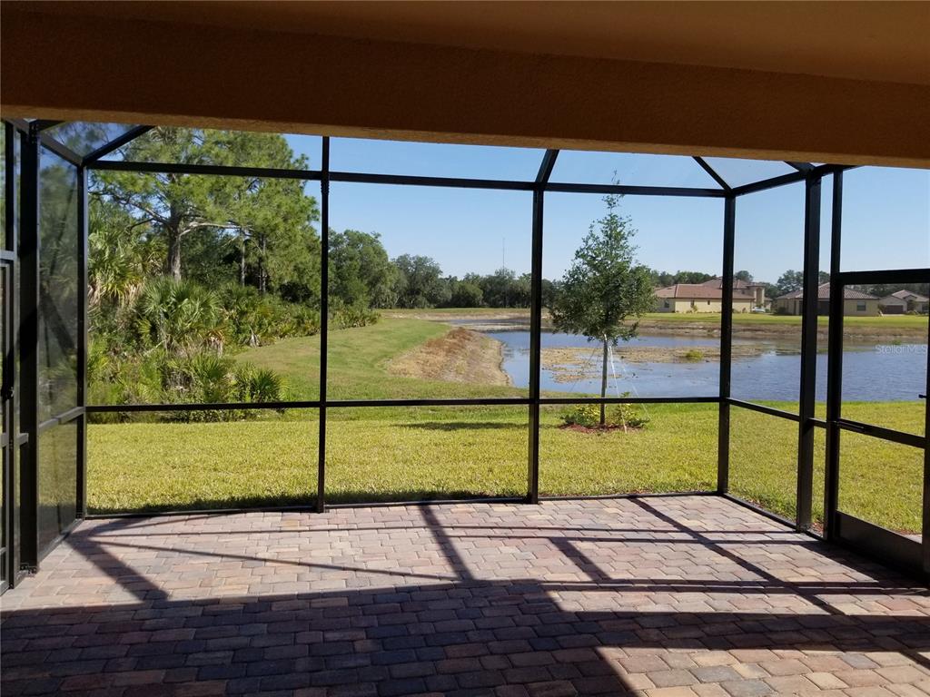 A screened-in brick patio overlooks a grassy lawn, a small pond, and distant houses — 12324 CANAVESE LANE, VENICE, FL