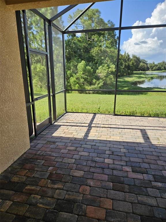 A screened-in patio with paver flooring overlooks a grassy lawn and a small pond — 12324 CANAVESE LANE, VENICE, FL