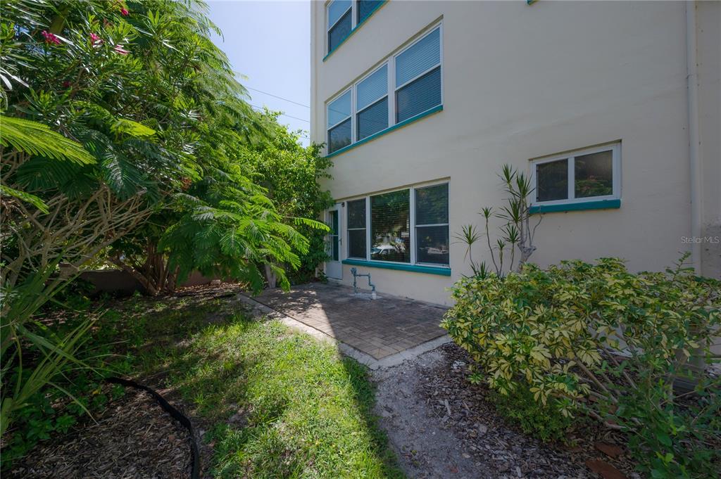 A paved patio sits beside a multi-story building with large windows and surrounding landscaping — 2960 59TH STREET S UNIT 101, GULFPORT, FL