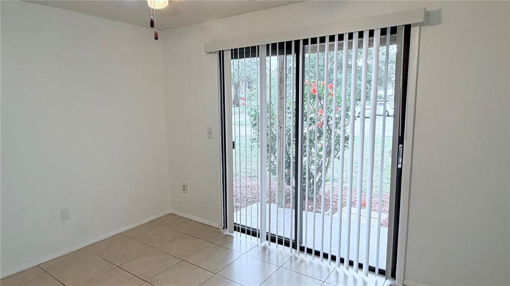 A room with light-colored tile flooring and vertical blinds covering a sliding glass door — 131 SABAL COURT UNIT E, OLDSMAR, FL
