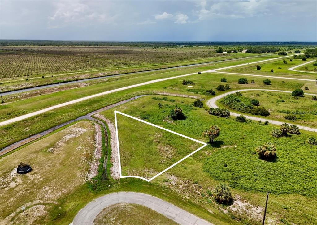 An aerial view shows a vacant, triangular-shaped plot of land bordered by a road and canal — 216 LYNBROOK LOOP, LABELLE, FL