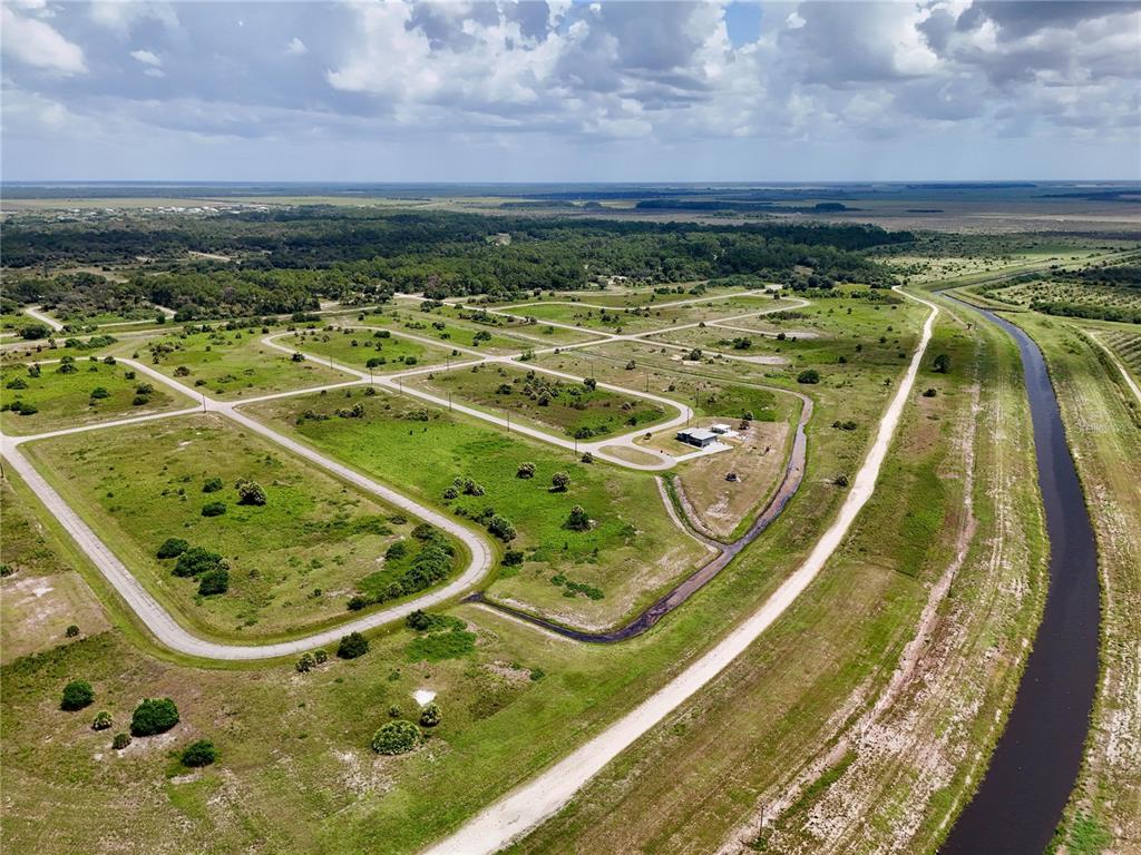 An aerial view shows a rural subdivision with paved roads, vacant lots, and a canal — 216 LYNBROOK LOOP, LABELLE, FL