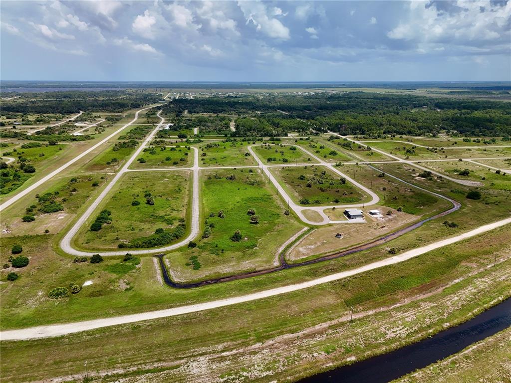 An aerial view shows a rural subdivision with paved roads, vacant lots, and a canal — 216 LYNBROOK LOOP, LABELLE, FL