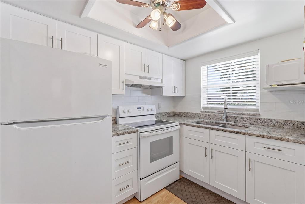 A kitchen with white cabinets, granite countertops, white appliances, and a ceiling fan — 404 E ORLANDO AVENUE UNIT 11B, OCOEE, FL