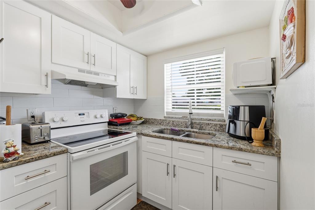 A kitchen features white cabinets, granite countertops, a white stove, and a window above the sink — 404 E ORLANDO AVENUE UNIT 11B, OCOEE, FL