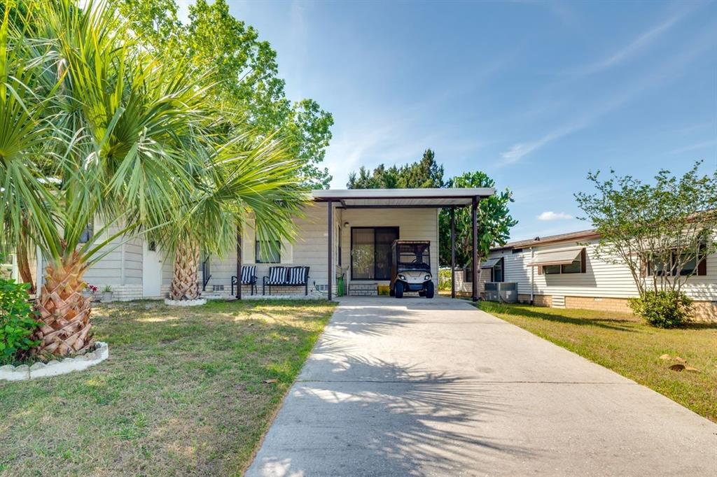 A single-story mobile home with a concrete driveway, carport, and a palm tree in front — 1224 DUSTIN DRIVE, LADY LAKE, FL