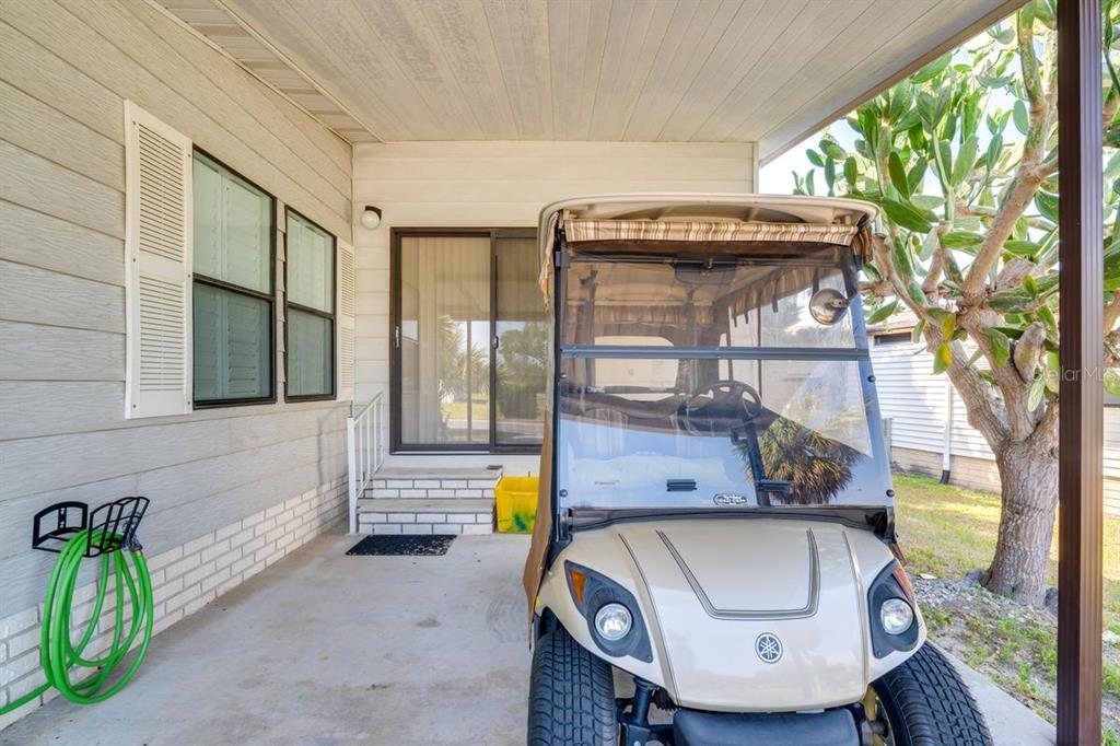 A beige golf cart is parked on a concrete patio beside a house exterior — 1224 DUSTIN DRIVE, LADY LAKE, FL