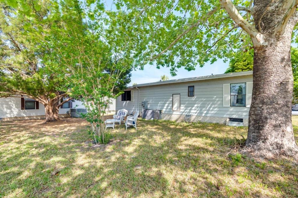 A backyard view of a single-story house with light gray siding and a large tree — 1224 DUSTIN DRIVE, LADY LAKE, FL