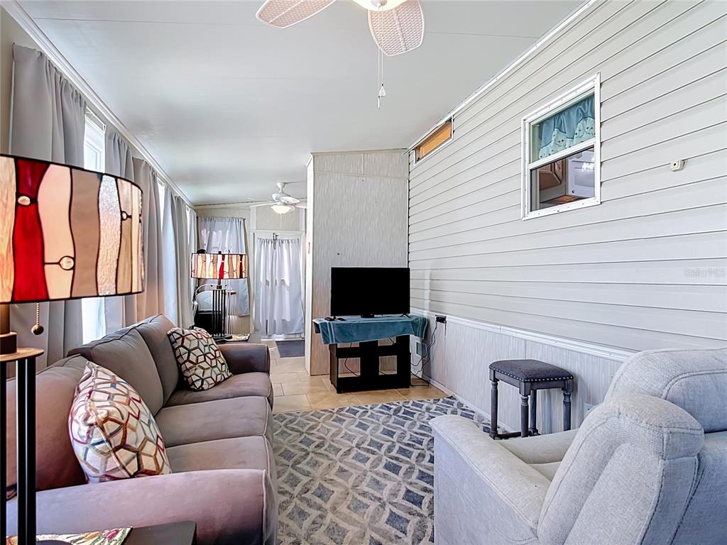 A sunroom with a gray sofa, recliner, patterned rug, and steps leading into the home — 9000 US HWY 192 UNIT 81, CLERMONT, FL